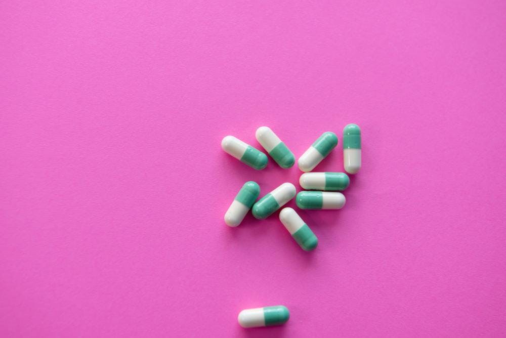 White and blue pills on a pink background