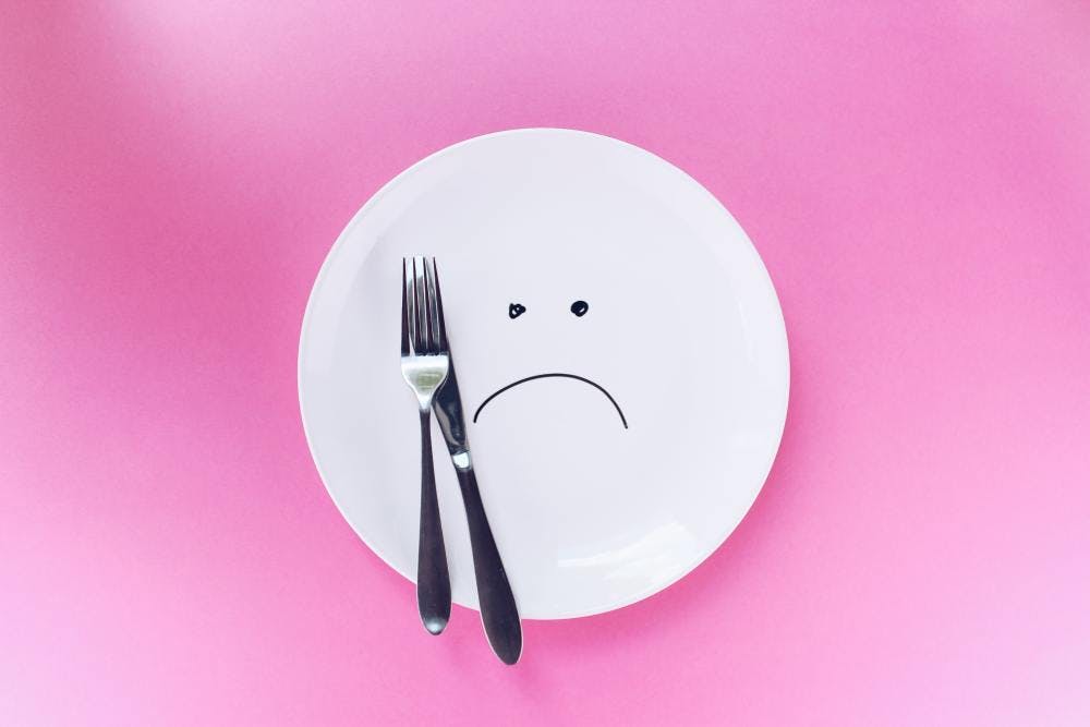 A plate with a sad face drawn on it and a fork & knife