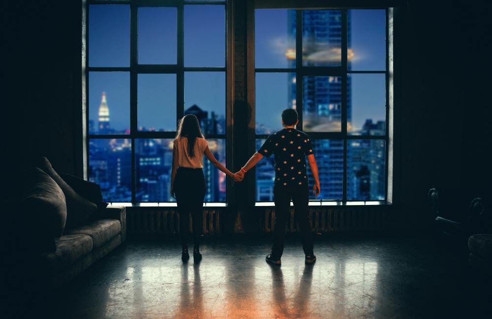 Two people holding hands in front of a large window