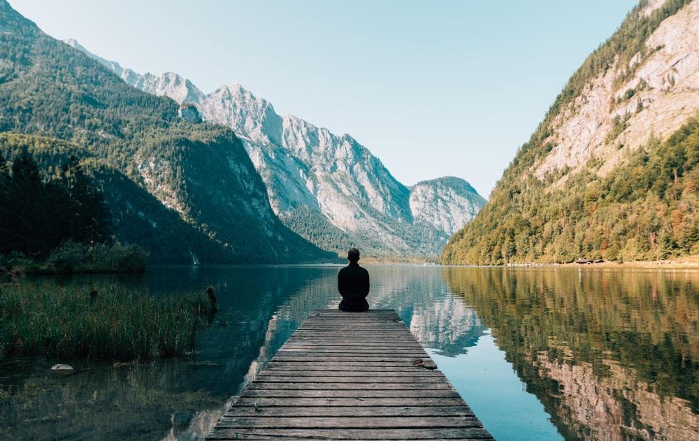 Someone meditating in front of water and mountains