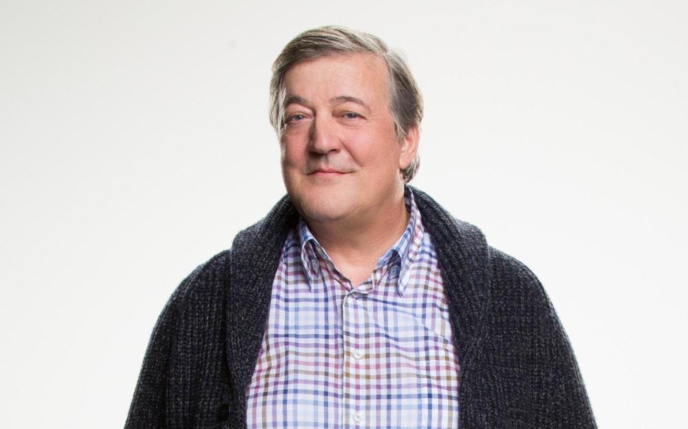 Stephen Fry smiling and wearing a checkered shirt and cardigan